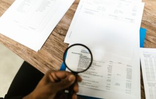 Close-up of hand using magnifying glass to review documents. Ideal for financial themes.