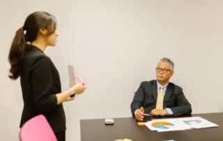 A professional woman presenting to a colleague during a business meeting in an office setting.