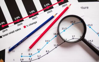 Magnifying glass and colored pencils on financial trend graphs highlighting sales growth.