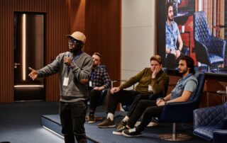 A group of diverse men engaging in a business conference with a speaker holding a microphone.