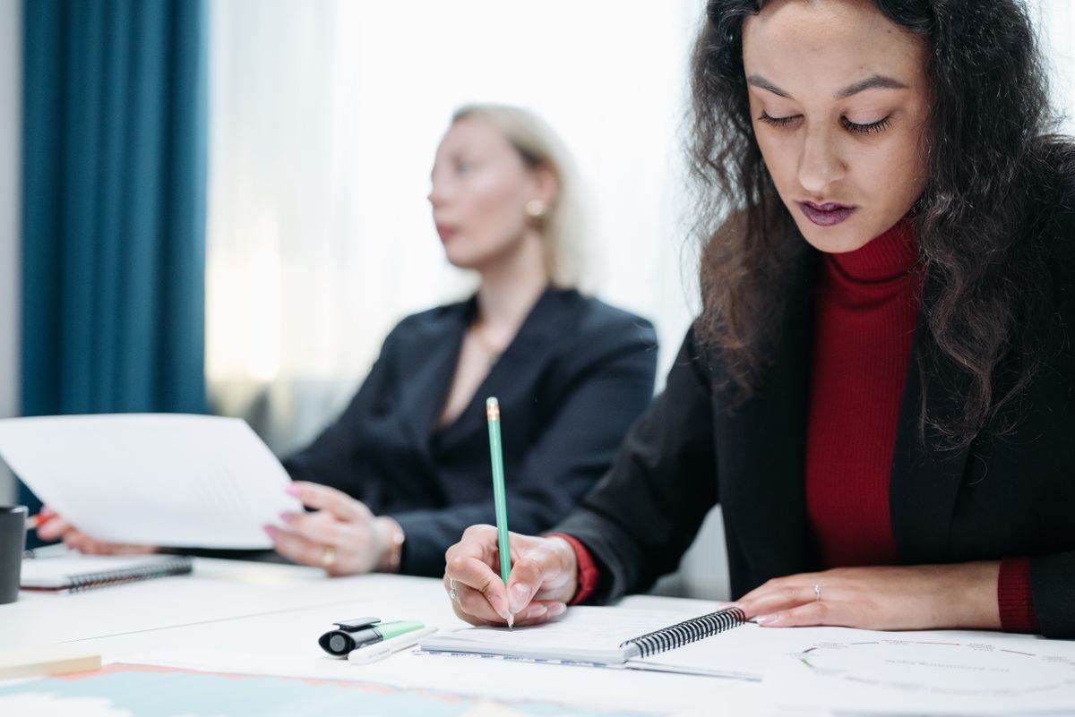 Two business women focused on taking notes during a meeting, highlighting professional diligence.
