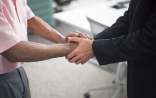 Close-up of a formal handshake between two businessmen in an office environment.