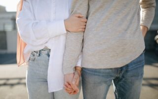 A close-up view of a couple holding hands and wearing casual attire outdoors.