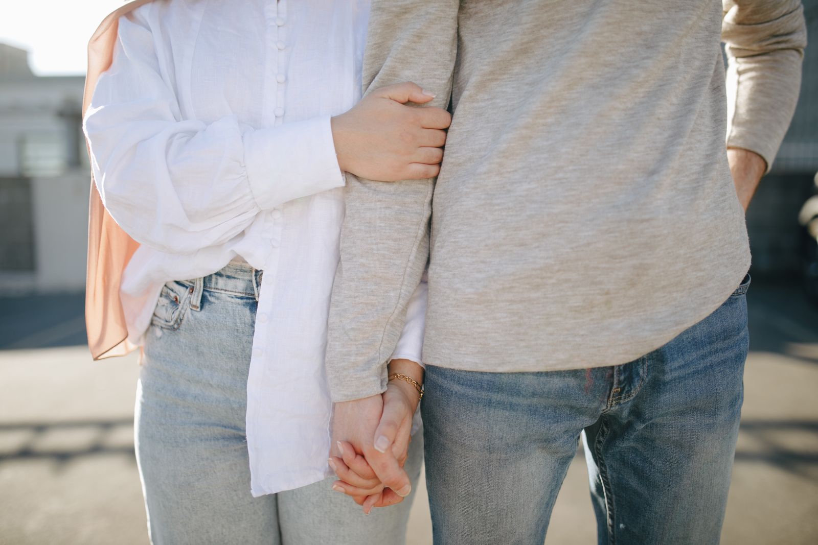 A close-up view of a couple holding hands and wearing casual attire outdoors.