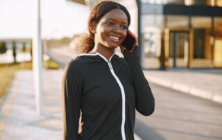 Young woman in sportswear smiling while talking on her smartphone outdoors.