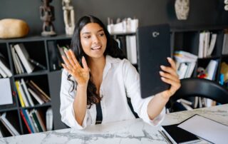 A young woman with henna on her hand video calling using a tablet in a modern office setting.