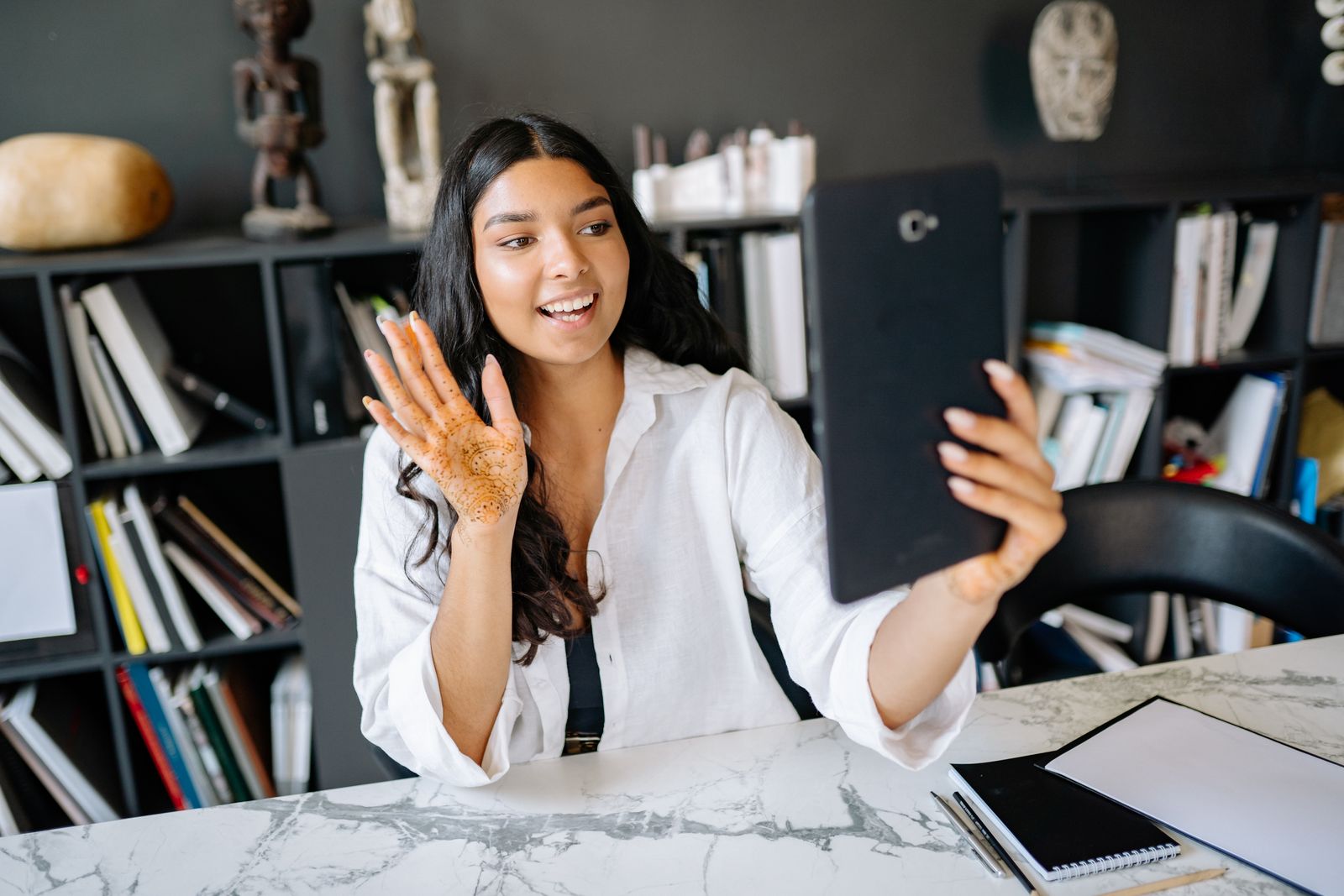 A young woman with henna on her hand video calling using a tablet in a modern office setting.