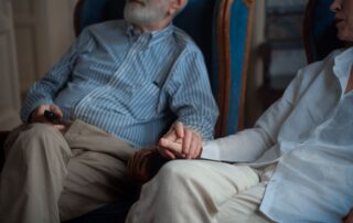 An elderly couple sitting together, holding hands in a cozy room, symbolizing companionship.