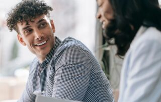 Caucasian man and black woman sharing a friendly smile indoors with natural light.