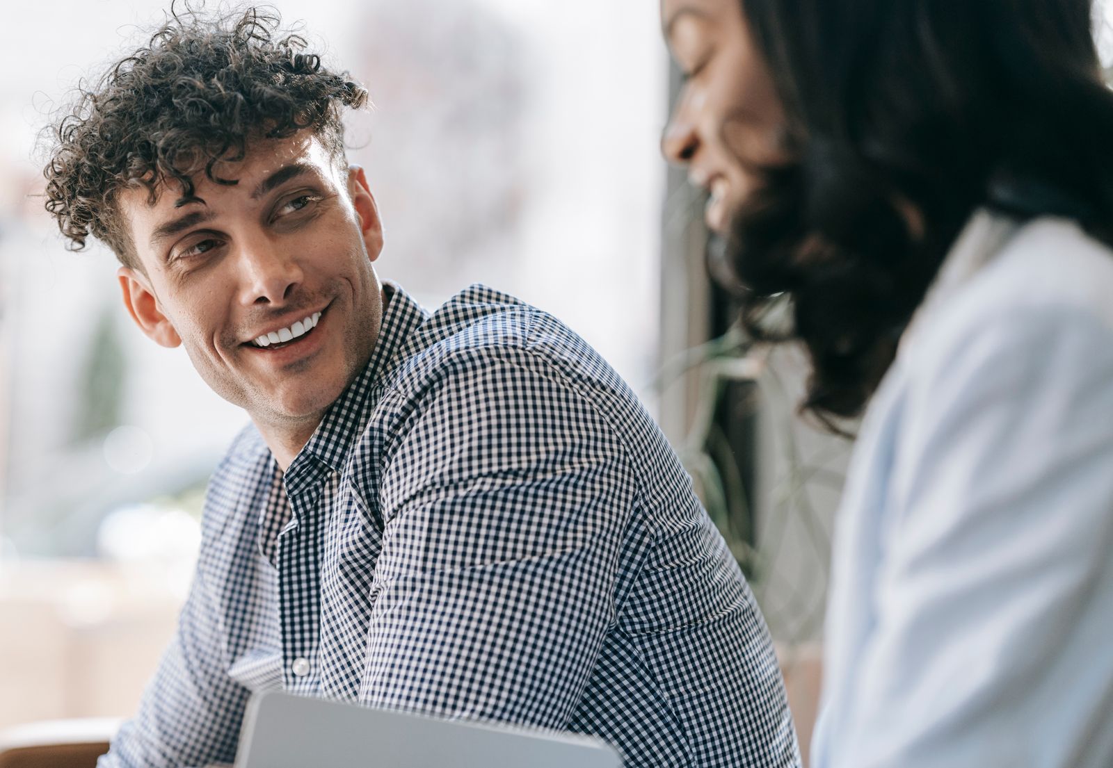 Caucasian man and black woman sharing a friendly smile indoors with natural light.