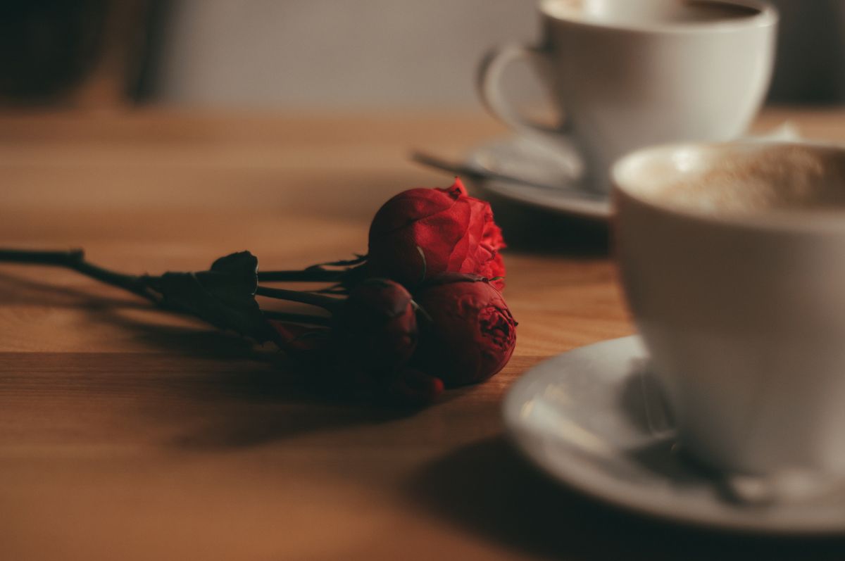 Two cups of coffee on a wooden table beside red roses