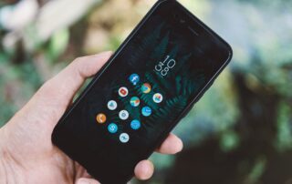 Close-up of a hand holding a smartphone with app icons and a nature wallpaper.